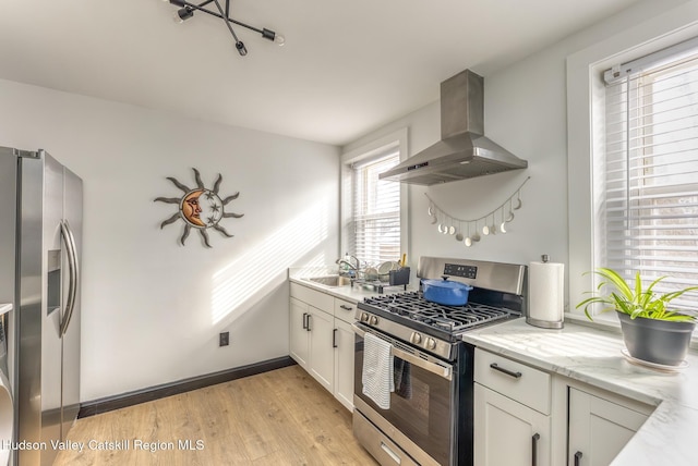 kitchen featuring baseboards, a sink, light wood-style floors, wall chimney range hood, and appliances with stainless steel finishes