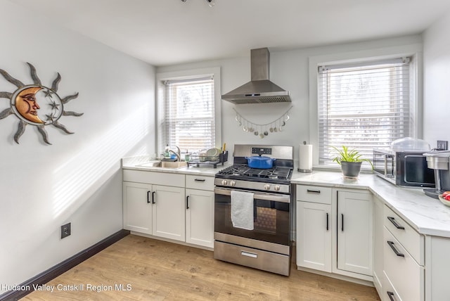 kitchen with white cabinets, stainless steel gas range, a sink, light wood-type flooring, and wall chimney range hood