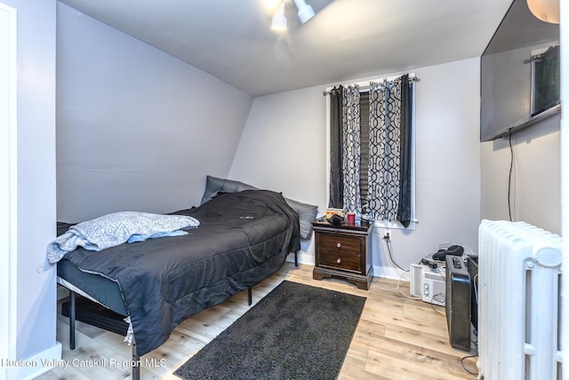 bedroom featuring baseboards, light wood-style flooring, and radiator heating unit