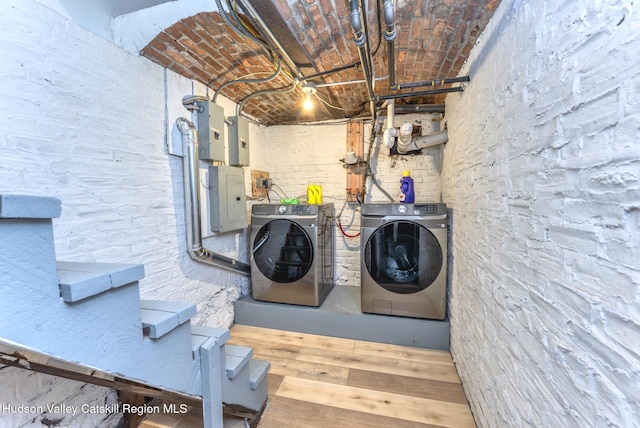 laundry area featuring electric panel, wood finished floors, washing machine and clothes dryer, laundry area, and brick ceiling