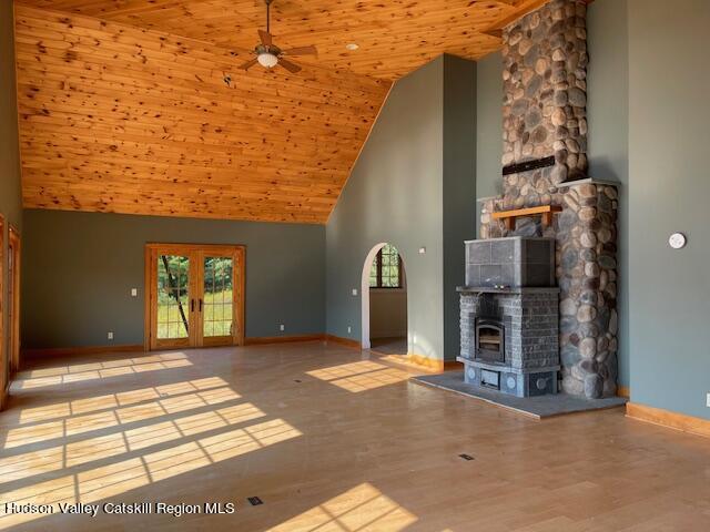 unfurnished living room featuring wood ceiling, ceiling fan, light hardwood / wood-style flooring, high vaulted ceiling, and a wood stove