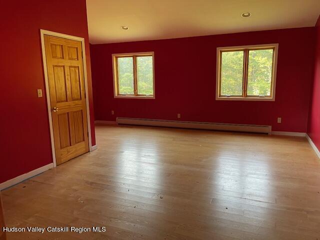 empty room with light wood-type flooring, baseboard heating, and plenty of natural light