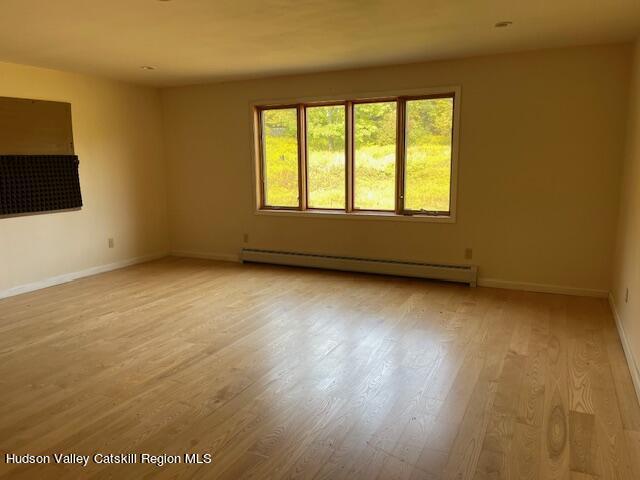 unfurnished room with light hardwood / wood-style floors and a baseboard heating unit