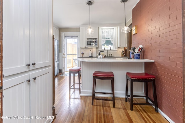 kitchen with white cabinets, hardwood / wood-style flooring, a breakfast bar area, stainless steel microwave, and a peninsula