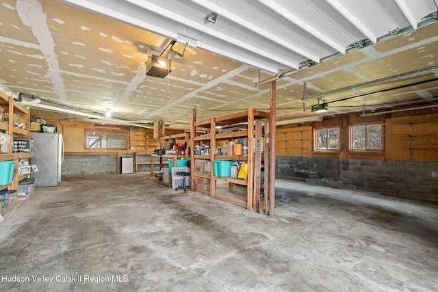garage with concrete block wall, freestanding refrigerator, and a garage door opener