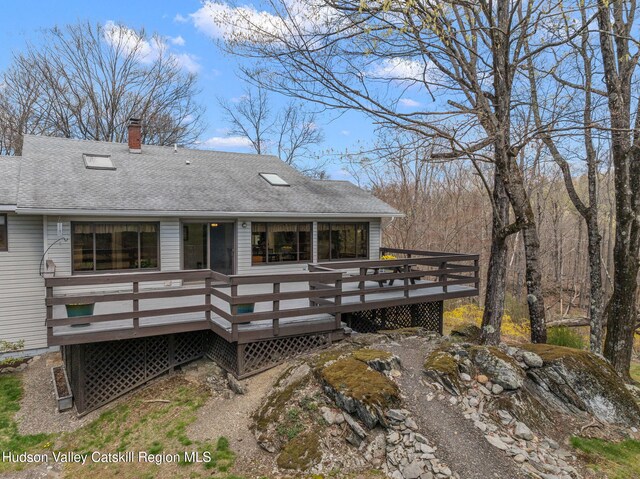 back of property featuring a deck, a shingled roof, and a chimney