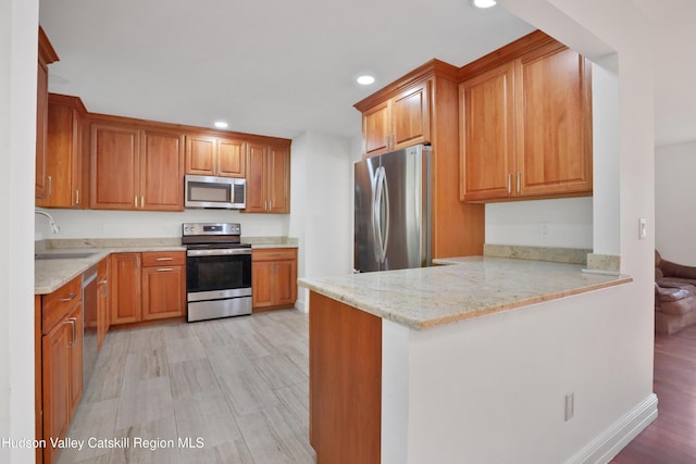 kitchen with kitchen peninsula, light wood-type flooring, stainless steel appliances, and sink