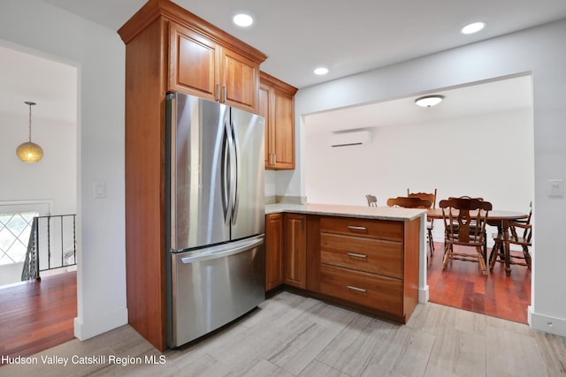 kitchen with kitchen peninsula, a wall unit AC, decorative light fixtures, light hardwood / wood-style floors, and stainless steel refrigerator