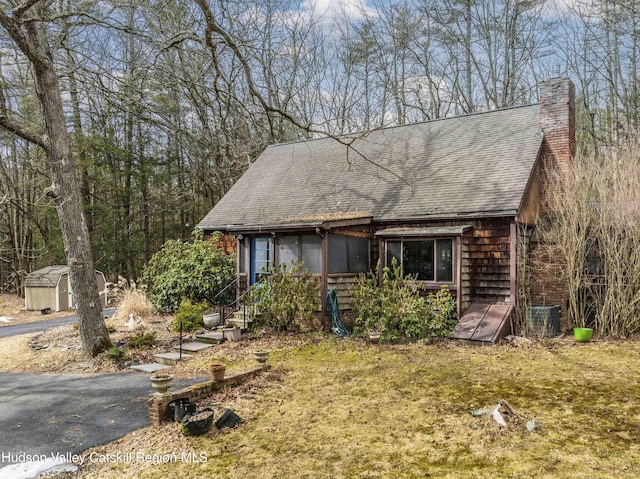 rustic home featuring an outbuilding, a chimney, a storage unit, and roof with shingles