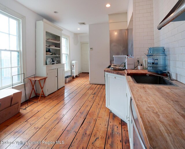 230 Warren St, Hudson, NY 12534 - kitchen with radiator heating unit, butcher block countertops, light wood-style flooring, a sink, and white cabinets