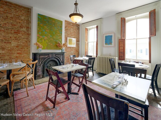 230 Warren St, Hudson, NY 12534 - dining space featuring radiator heating unit, brick wall, wood finished floors, and a fireplace