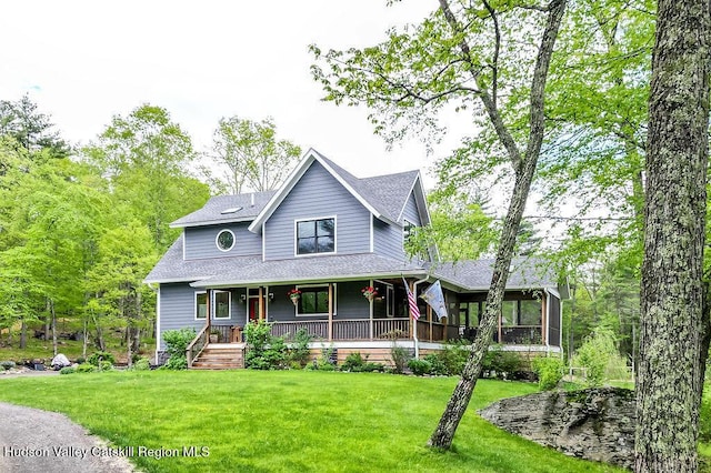 view of front of home with roof with shingles, covered porch, a front lawn, and a sunroom