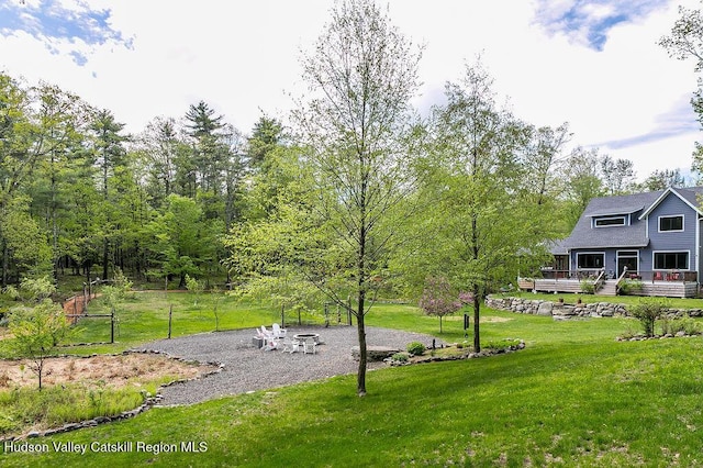 view of green lawn featuring a wooden deck and an outdoor fire pit