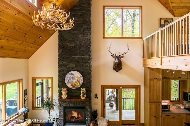 living area featuring high vaulted ceiling, wooden ceiling, a fireplace, a chandelier, and healthy amount of natural light