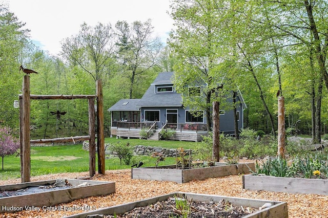 back of property featuring a vegetable garden, a lawn, a deck, and roof with shingles