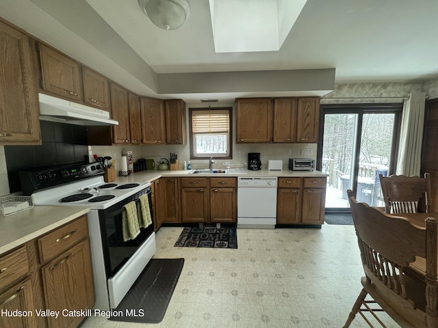 kitchen featuring sink, backsplash, white appliances, and a skylight