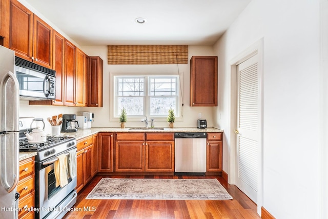 kitchen featuring hardwood / wood-style flooring, light stone countertops, appliances with stainless steel finishes, and sink