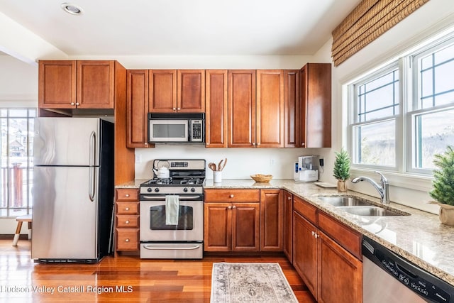 kitchen featuring stainless steel appliances, light stone countertops, sink, and light hardwood / wood-style floors