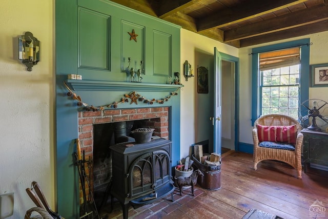 living area featuring beamed ceiling, a wood stove, hardwood / wood-style flooring, wooden ceiling, and baseboards