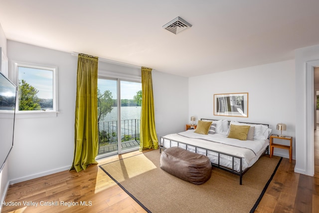 bedroom with a water view, light wood-type flooring, access to outside, and multiple windows