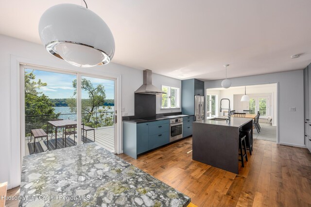 kitchen featuring hanging light fixtures, a healthy amount of sunlight, wall chimney range hood, and appliances with stainless steel finishes