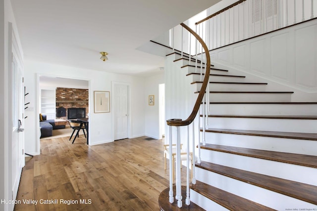 stairway with wood-type flooring and a brick fireplace