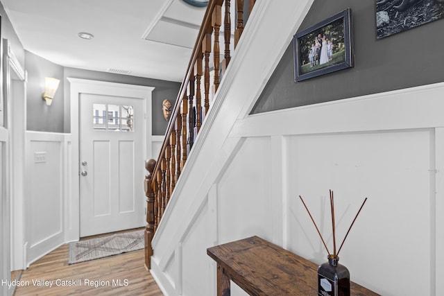 entryway featuring a wainscoted wall, visible vents, light wood-style floors, stairway, and a decorative wall