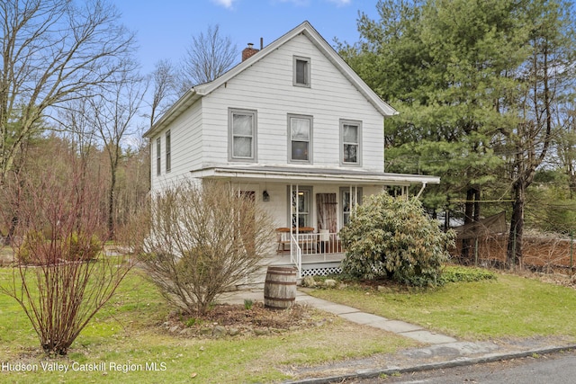 view of front of home with a chimney, covered porch, and a front yard