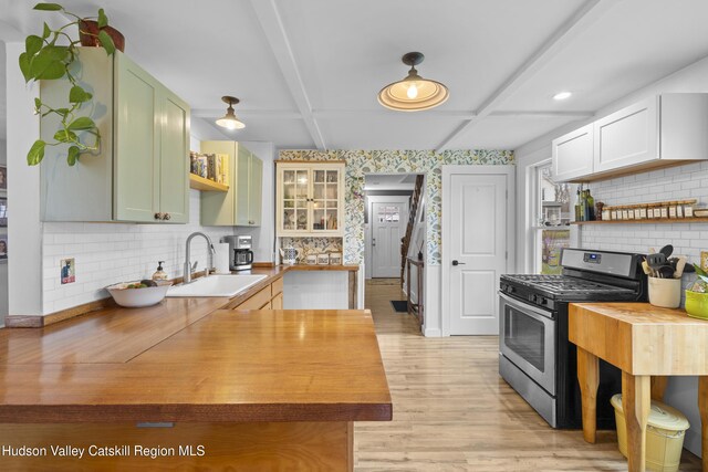 kitchen featuring butcher block countertops, open shelves, stainless steel gas range oven, and a sink