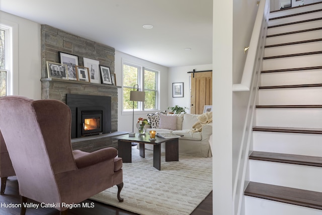 living room with a barn door, a stone fireplace, and hardwood / wood-style flooring