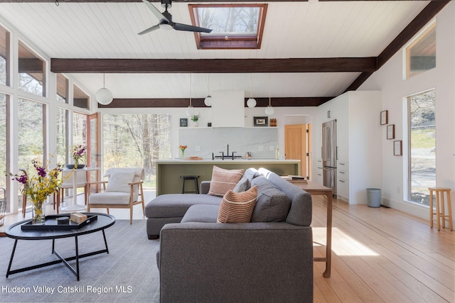 living room with a skylight, ceiling fan, light wood-type flooring, beam ceiling, and wood ceiling