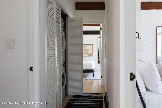 hallway featuring beamed ceiling, hardwood / wood-style flooring, and stacked washer and clothes dryer