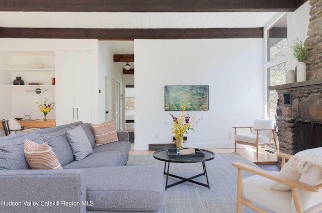 living room featuring beam ceiling, a fireplace, and light wood-type flooring