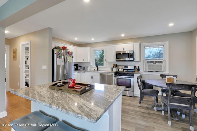 kitchen with light wood finished floors, a sink, light stone counters, white cabinets, and appliances with stainless steel finishes