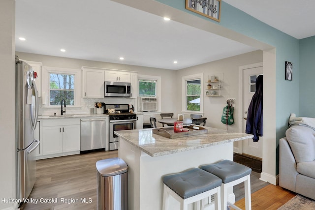 kitchen with light stone countertops, a sink, stainless steel appliances, light wood-type flooring, and a breakfast bar