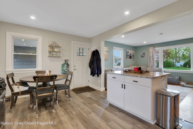 kitchen with recessed lighting, light stone counters, white cabinets, a center island, and light wood-type flooring