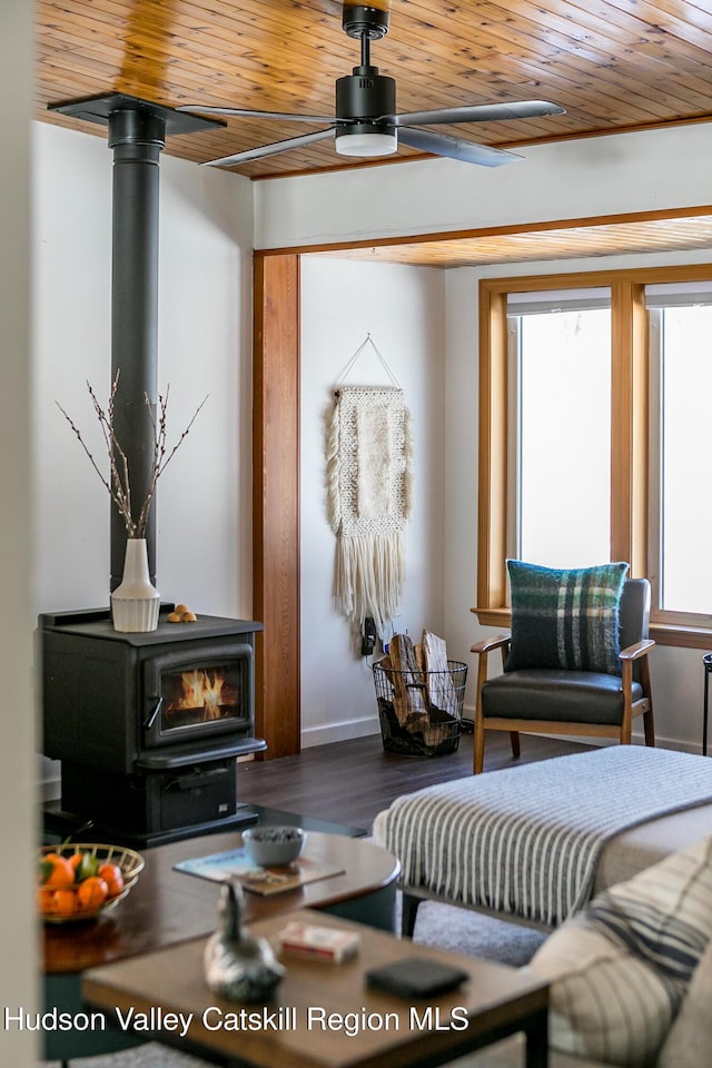 living room with wood ceiling, dark wood-type flooring, ceiling fan, and a wood stove