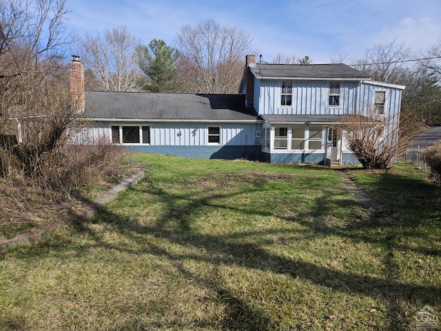 back of house featuring a chimney, a yard, covered porch, and board and batten siding