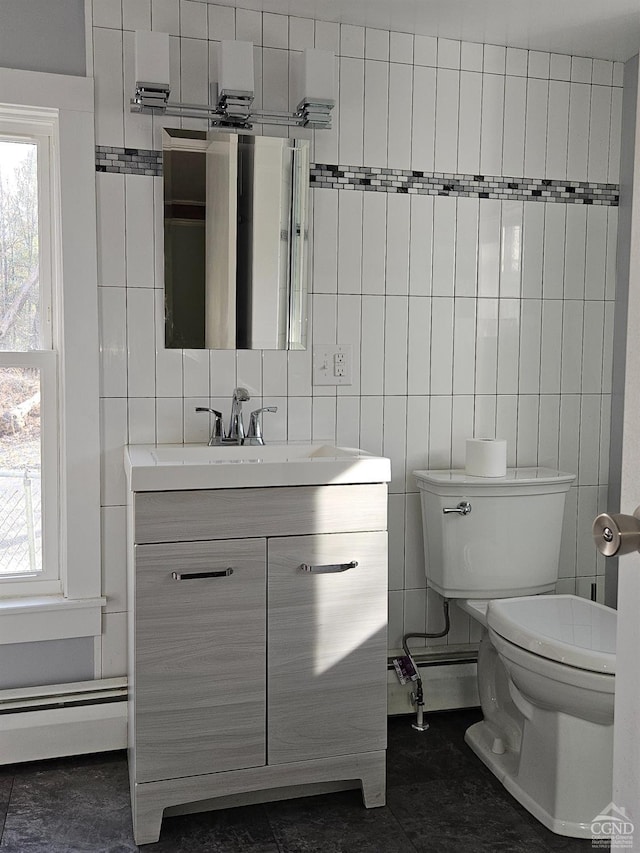 bathroom featuring toilet, plenty of natural light, vanity, tile walls, and a baseboard heating unit