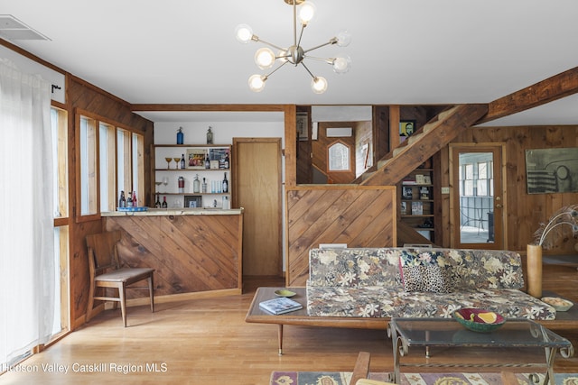 living area with visible vents, light wood-type flooring, a chandelier, wooden walls, and bar area