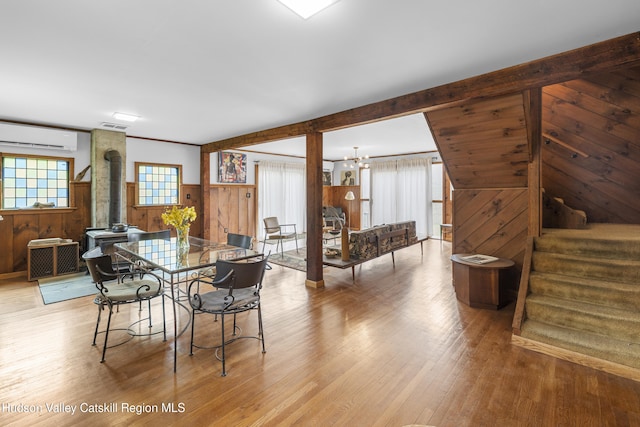 dining space with wainscoting, a wood stove, light wood-type flooring, an AC wall unit, and wooden walls