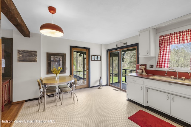 kitchen featuring a sink, baseboards, white cabinetry, and a wealth of natural light