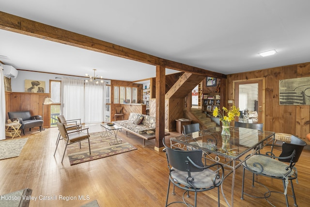 dining space with an AC wall unit, wood walls, wood finished floors, and an inviting chandelier