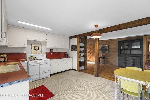kitchen featuring double oven range, hanging light fixtures, a sink, white cabinets, and wooden walls
