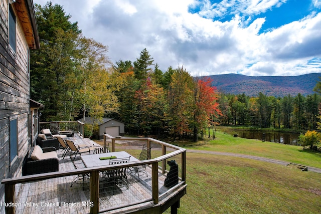 wooden deck featuring a garage, an outbuilding, a yard, and a water and mountain view