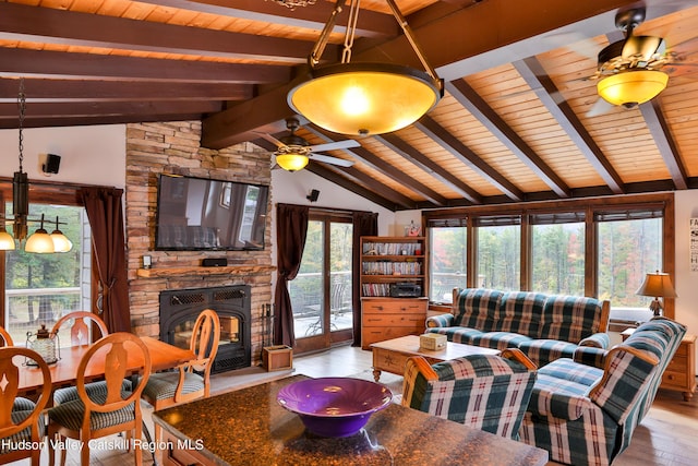 living room with lofted ceiling with beams, light hardwood / wood-style floors, a stone fireplace, and wood ceiling