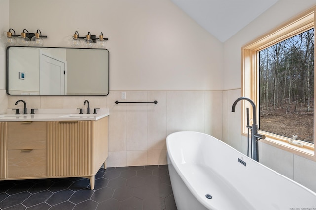 bathroom with tile patterned floors, lofted ceiling, a bathtub, vanity, and tile walls