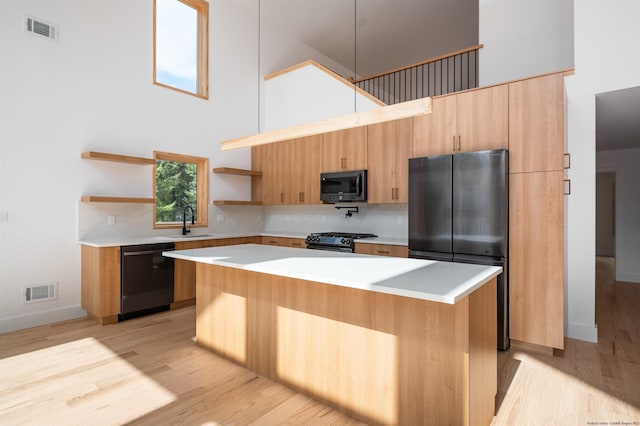 kitchen with black appliances, sink, a kitchen island, a towering ceiling, and light hardwood / wood-style floors