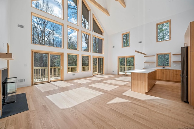 unfurnished living room with beamed ceiling, light hardwood / wood-style flooring, high vaulted ceiling, and sink