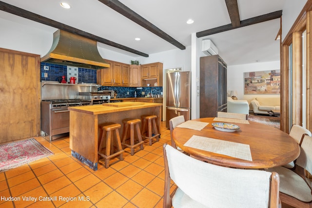 kitchen with wood counters, appliances with stainless steel finishes, tasteful backsplash, exhaust hood, and beamed ceiling